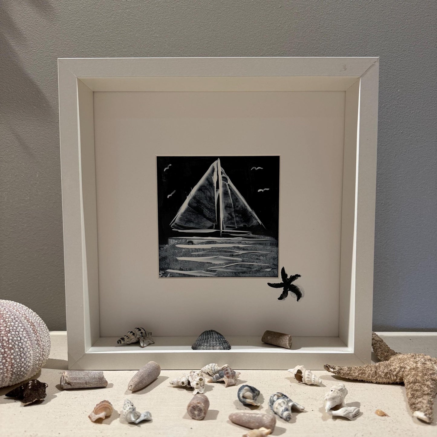 Ein gerahmtes Kunstwerk mit einem Schwarz-Weiß-Gemälde eines Segelboots. Das Gemälde ist vor einem schwarzen Hintergrund