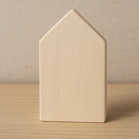 Ein kleiner, hellfarbiger Holzblock in Hausform. Der Block hat ein schlichtes, minimalistisches Design mit einem Satteldach