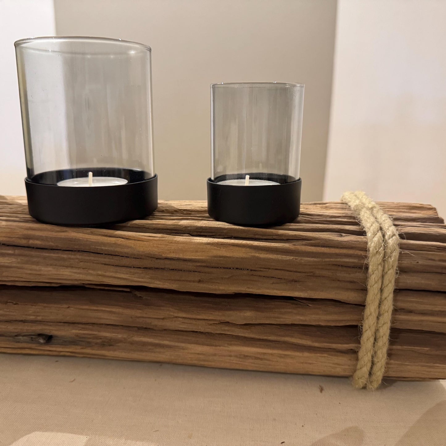 Ein dekorativer Kerzenhalter mit zwei Glaszylindern, die jeweils eine brennende weiße Kerze in schwarzen Sockeln halten.