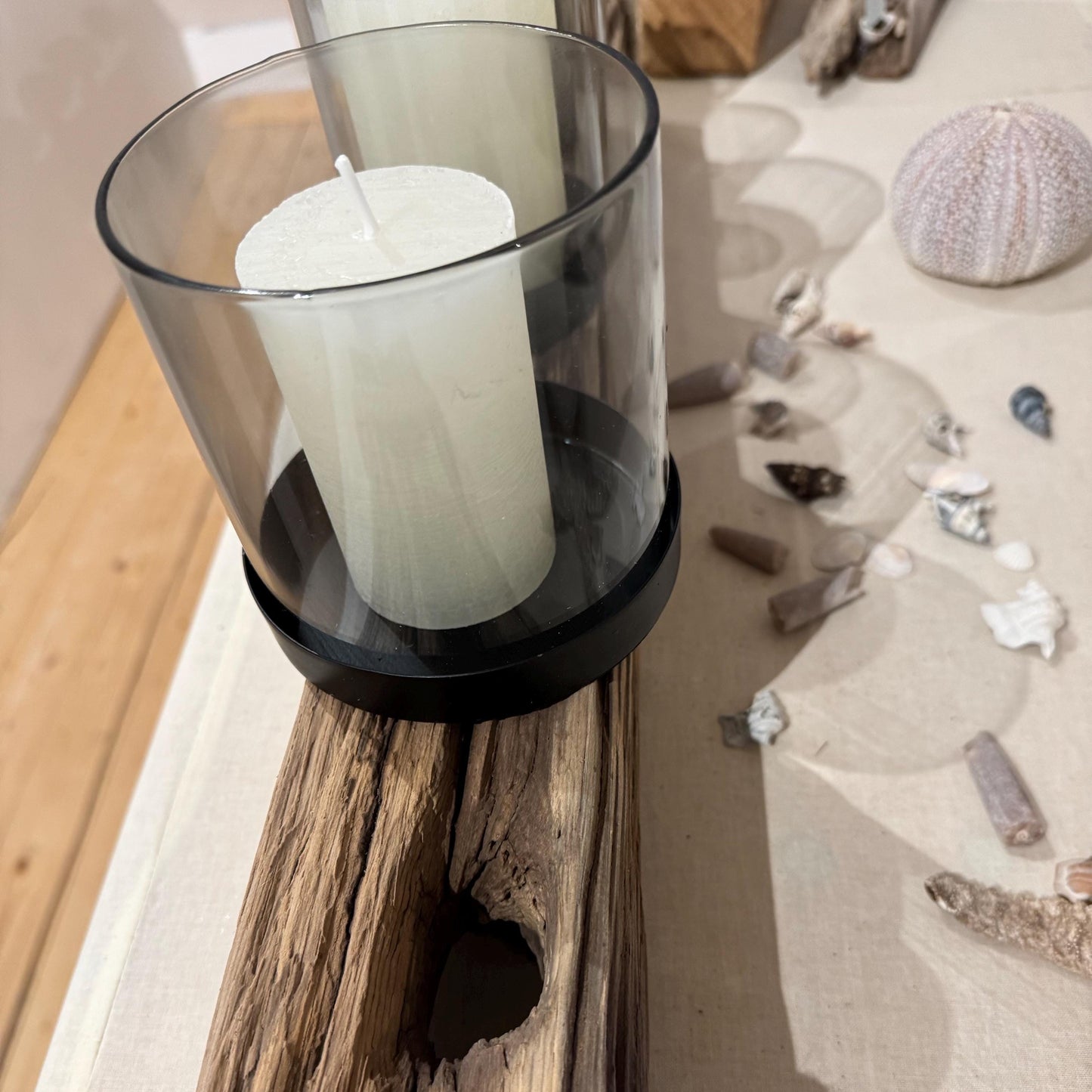 Ein rustikaler Kerzenhalter aus Holz mit vier weißen Säulenkerzen in Glas- und schwarzen Metallhaltern.