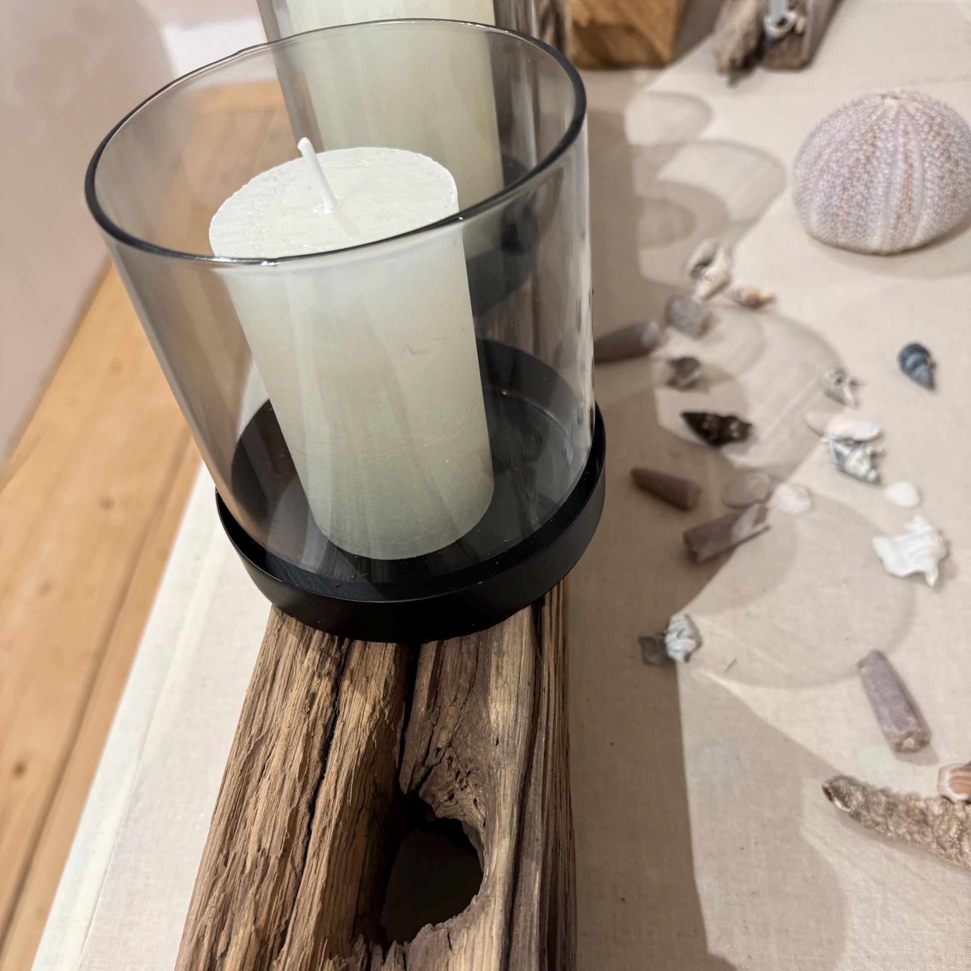 Ein rustikaler Kerzenhalter aus Holz mit vier weißen Säulenkerzen in Glas- und schwarzen Metallhaltern.