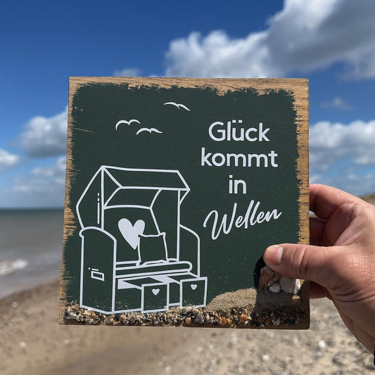 Holzschild Glück kommt in Wellen gehalten vor Strand, Meer und blauem Himmel.