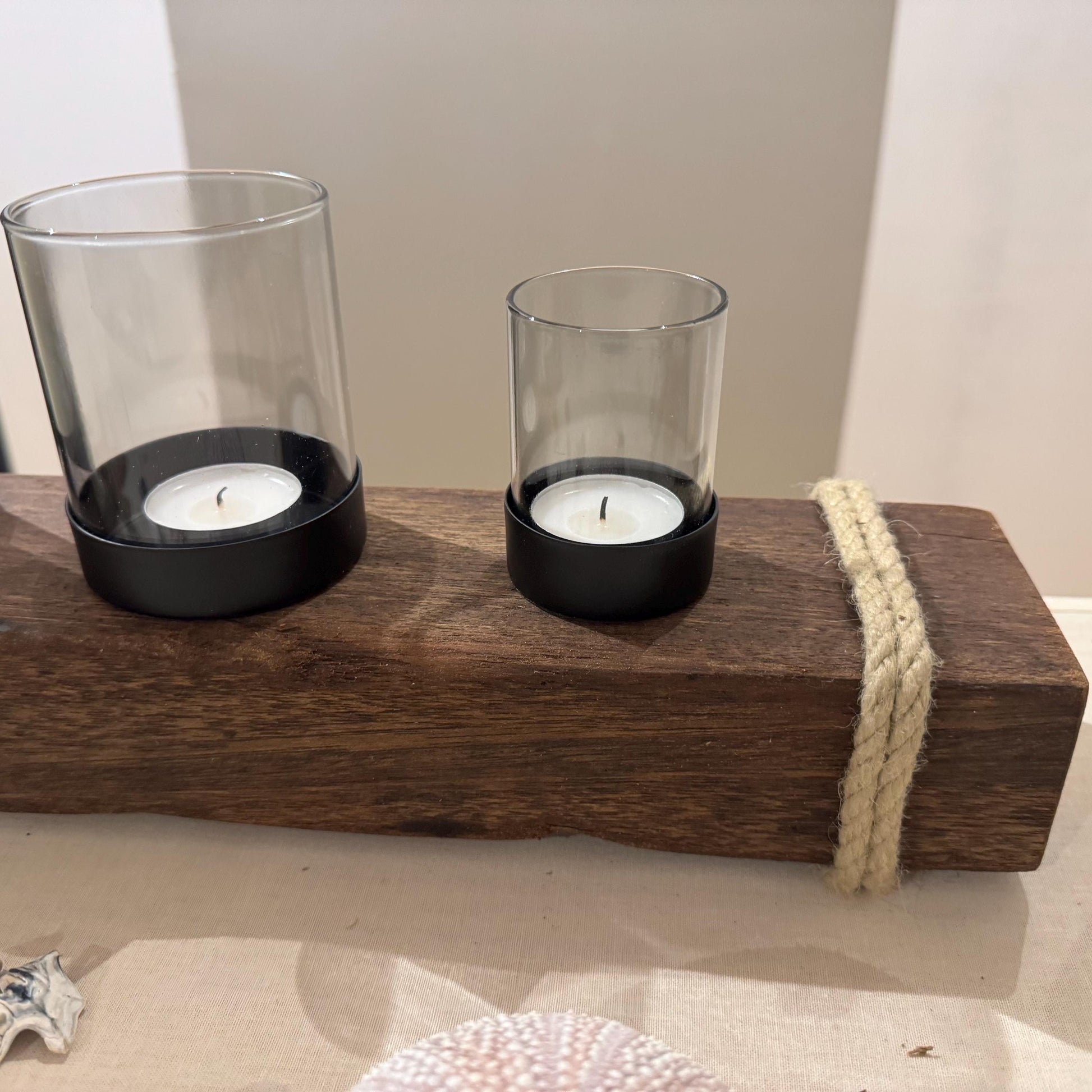 Ein dekorativer Kerzenhalter mit zwei Glaszylindern, die jeweils eine brennende weiße Kerze in schwarzen Sockeln halten.