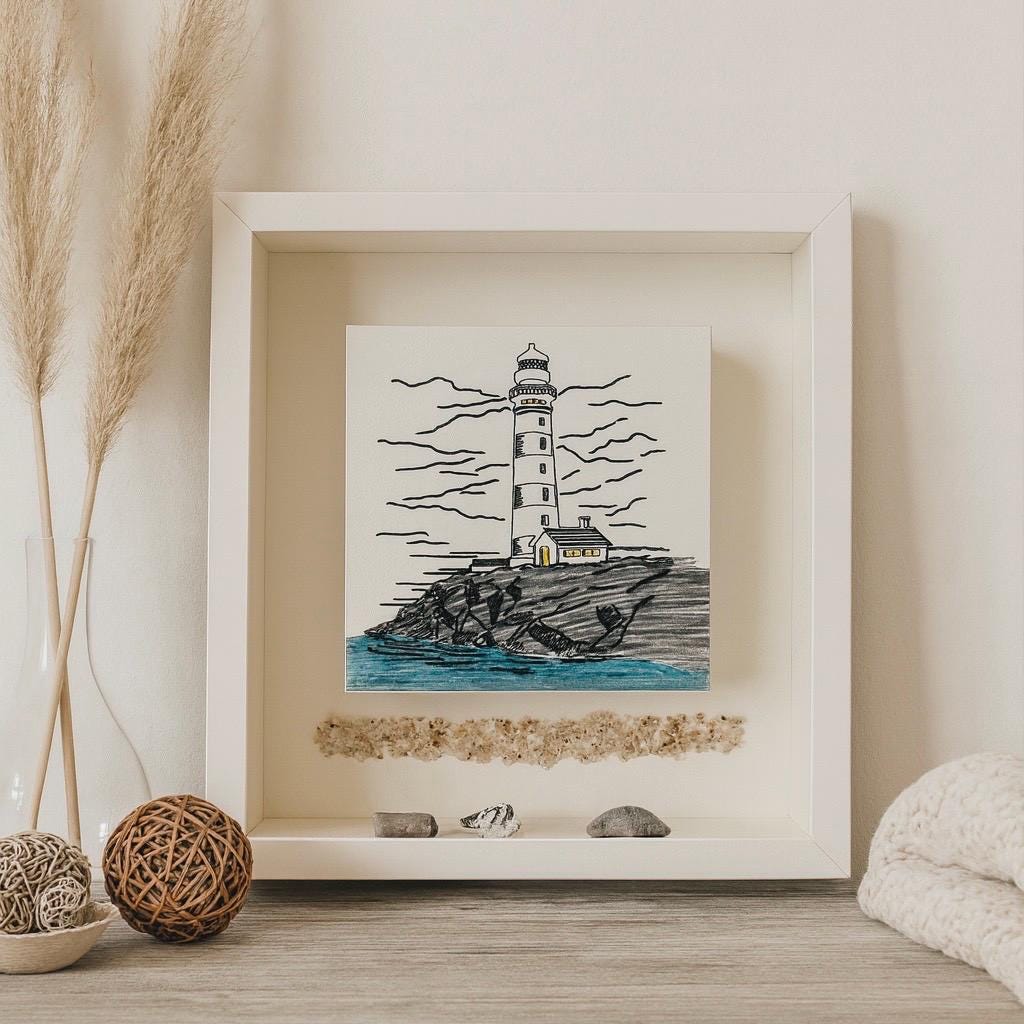 Maritime Wanddeko im weißen Holzrahmen: handgezeichnetes Leuchtturm-Bild - nordische Küstenkunst für natürliche Wohnräume.