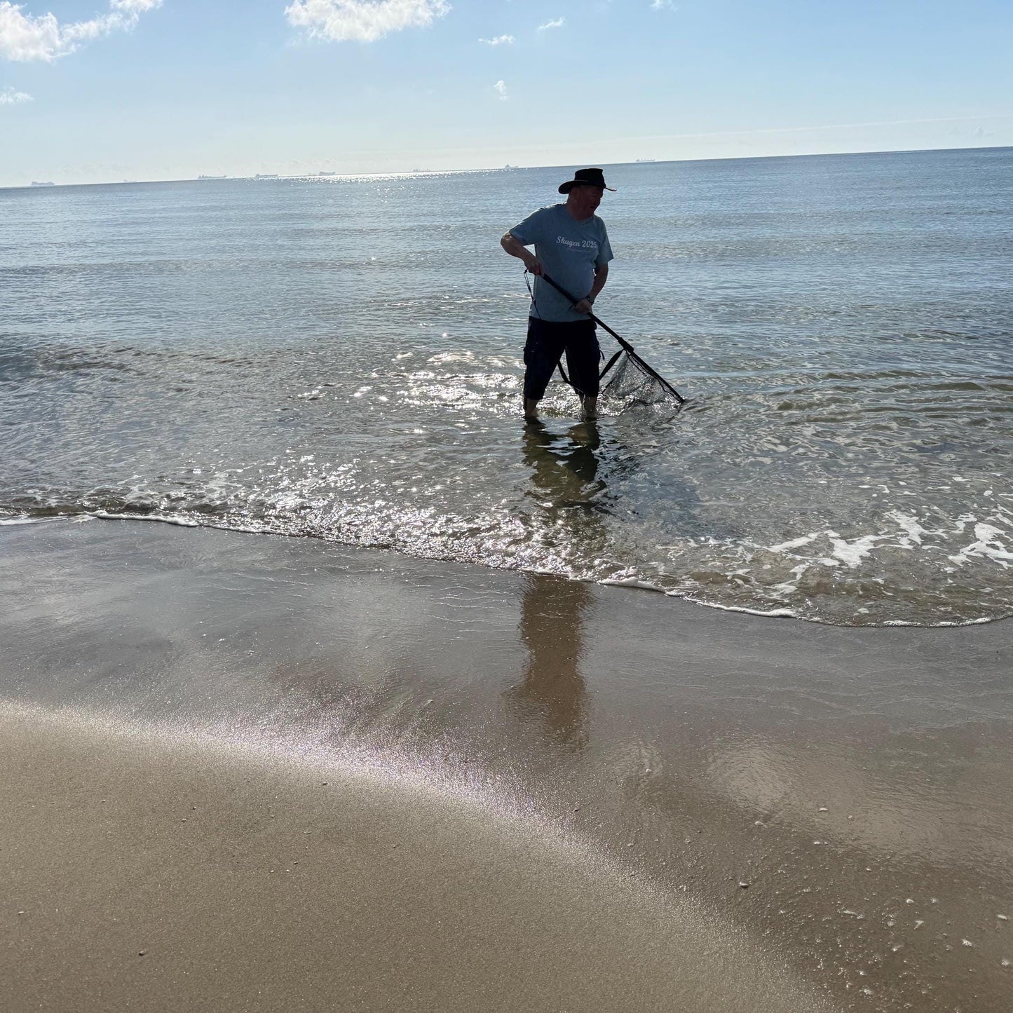 Eine Person steht im Meer mit einem Fischernetz, trägt einen Hut und ein hellblaues T-Shirt