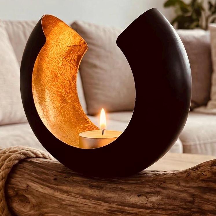 Nahaufnahme Design Lichtschale schwarz mit goldener Innenseite und brennendem Teelicht auf Treibholz Deko