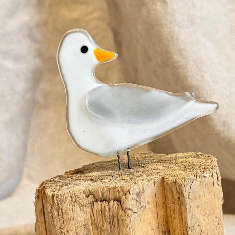 Seitenansicht weiße Glas Möwe mit hellgrauem Flügel und schwarzem Auge stehend auf Treibholz, skandinavische Küstendeko