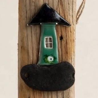Detailaufnahme grünes Fusing Glas Häuschen mit schwarzem Dach und weißem Fenster auf Treibholz